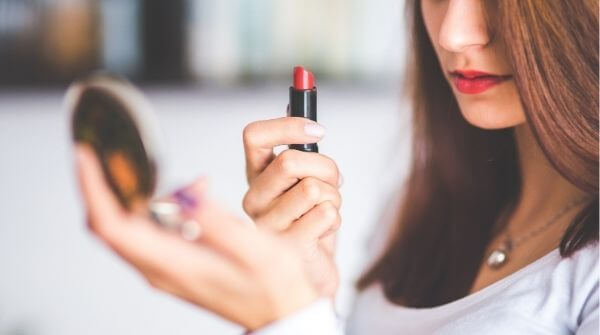 Woman putting red lipstick looking in the mirror. Red lipstick color is suitable for wedding or parties. 